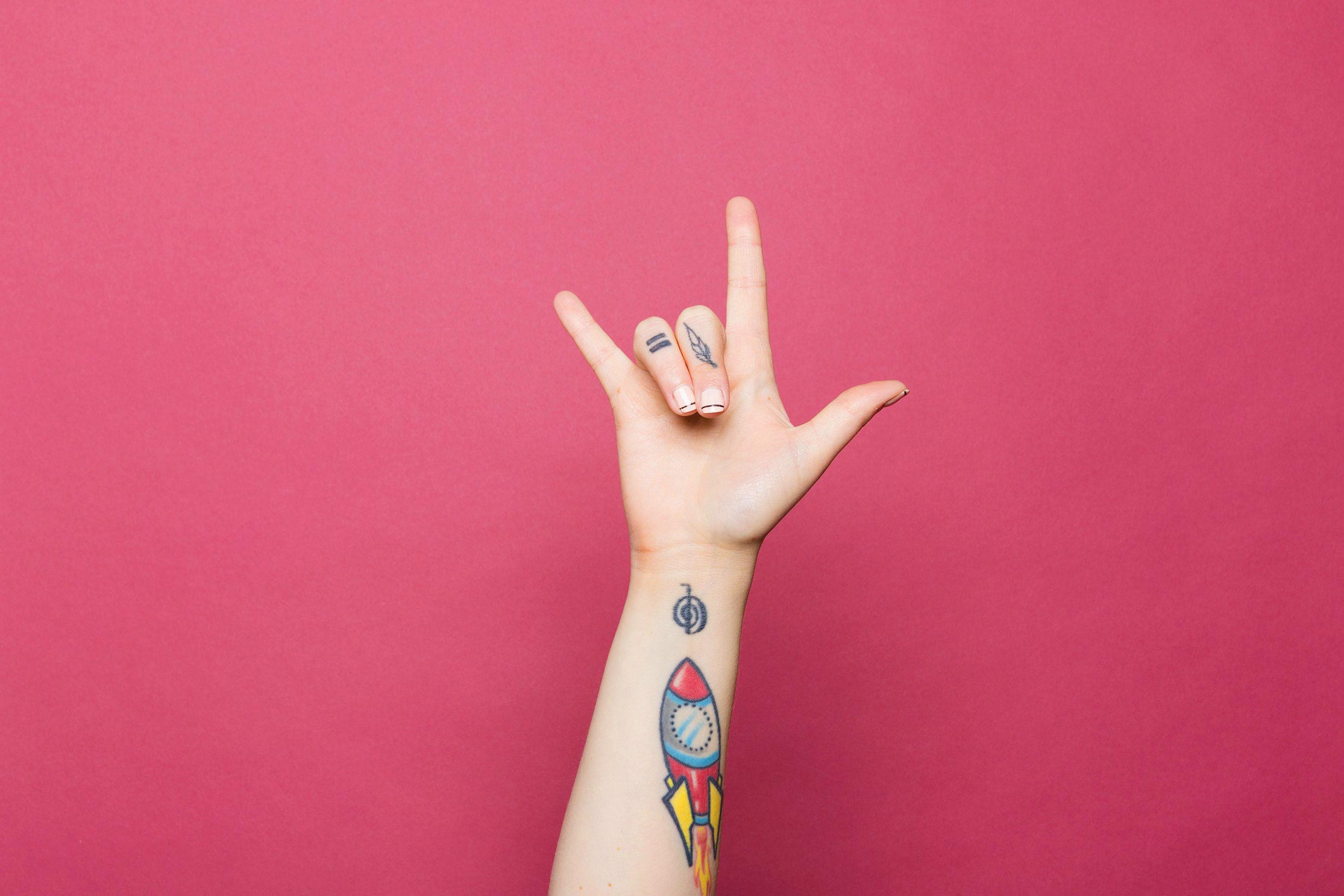 A photo of a tattooed hand, giving the "I love you" sign.
